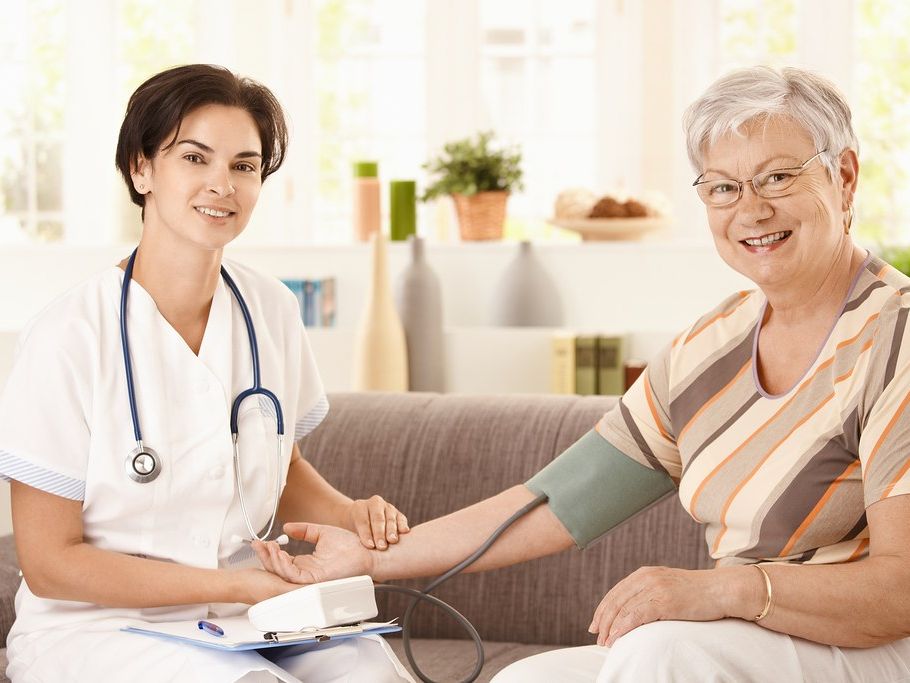 A home nurse checking an older woman’s blood pressure in her living room