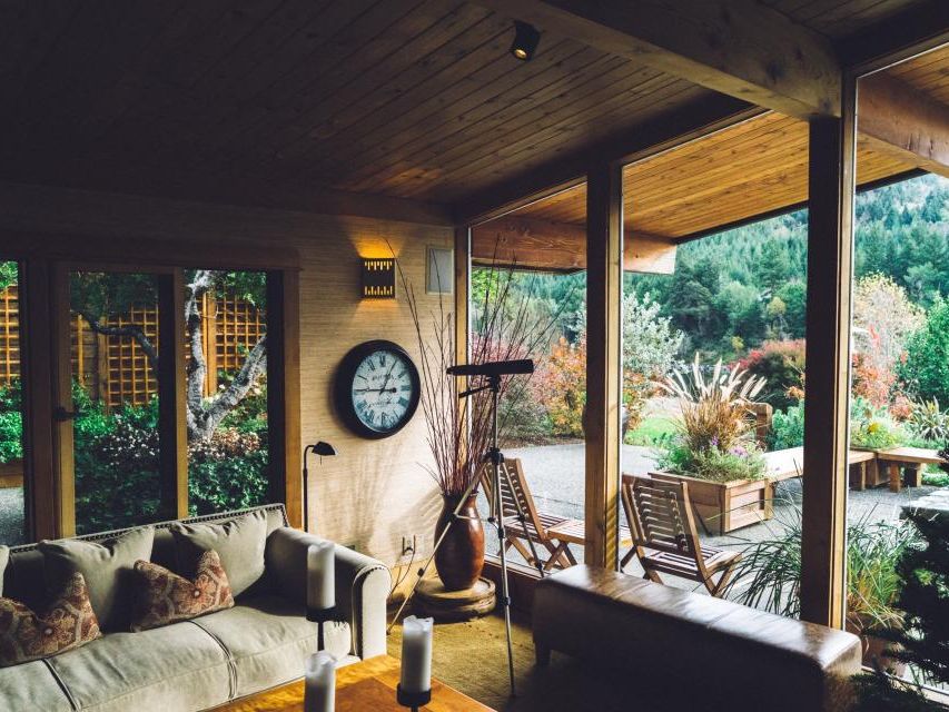 A lived-in sun room with a sofa, a wall clock and the garden through open doors