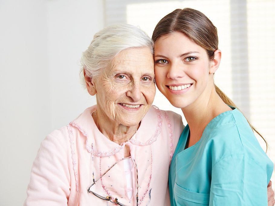 A caregiver with her arm around an older woman, both smiling