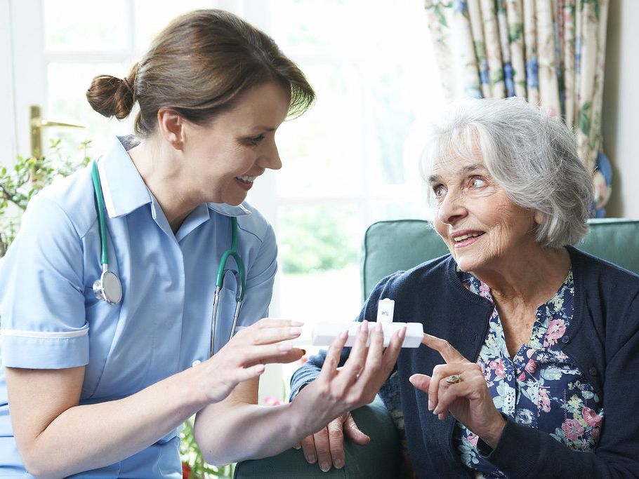 A nurse talking an older woman through her medication at home